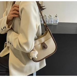 Detail of cream leather shoulder bag with dark brown trim and white monster charm accessory