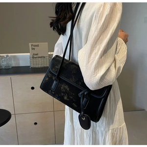 Detail view of retro black shoulder bag with gold texture on model with beige dress