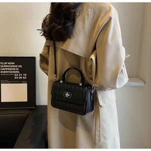 Detail of a black quilted crossbody bag with silver turn-lock clasp on a model