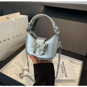Close-up of mini silver bow shoulder bag with chain strap in a premium gift box setup