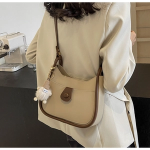 Detailed side view of beige bucket bag with brown trim and plush dwarf charm detail
