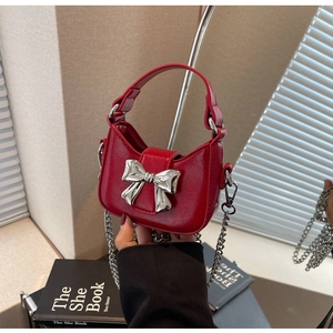 Close-up of mini red patent leather bag with silver bow accent and metal chain strap