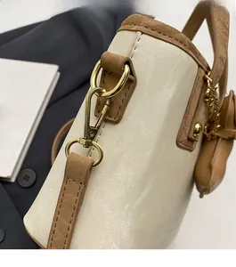Détail du fermoir en métal doré et de la bandoulière bicolore sur un sac crème