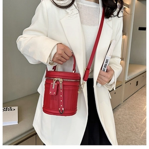 Detail of red leather barrel bag with gold hardware worn by model in white suit