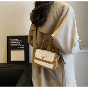 Close-up of quilted cream crossbody bag with brown trim on a woman wearing a trench coat