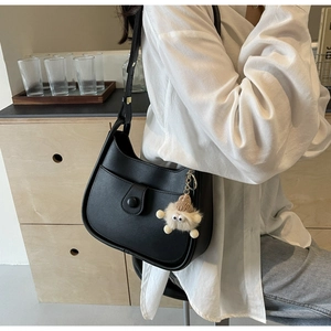 Detail of black faux leather bucket bag with plush charm and decorative button strap