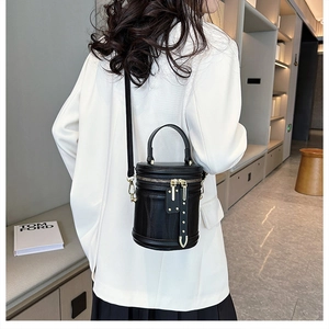 Detailed view of black cylindrical crossbody bag with vertical grain and gold hardware