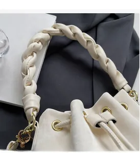 Detail of cream bucket bag featuring woven rope handle and gold eyelets on a clean desk