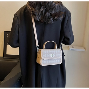 Close-up of beige quilted crossbody bag with metal twist lock and detachable shoulder strap