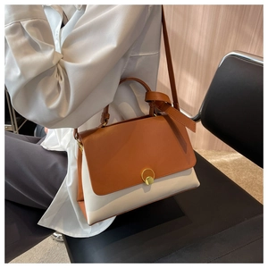 Detail of color-block shoulder bag featuring brown flap and cream body with gold buckle