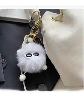 White fluffy monster bag charm with black eyes and gold hardware on a cream bag