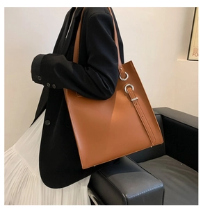 Detail view of large brown leather tote bag with silver metal ring and decorative straps