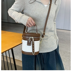 Detail of a brown and white cylinder bucket bag with silver zippers and adjustable strap