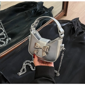 Detail of silver crossbody bag with a large metallic bow and detachable chain strap