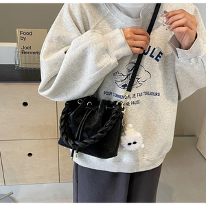 Detail of black faux leather bucket bag with woven handle and plush cat charm accessory