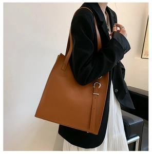 Detail of a large brown leather tote bag with silver metal buckles and long shoulder straps