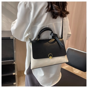 Detailed view of black and white contrast leather handbag with round gold buckle