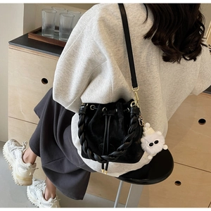 Detail of black suede bucket bag featuring woven handle and plush eye charm accessory