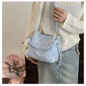 Sac seau bleu clair avec texture plissée, poignée tressée et charm pompon blanc