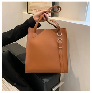 Detail of a brown leather tote bag with silver rings and decorative buckle straps