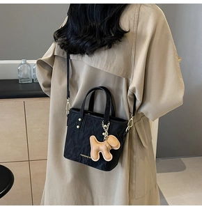 Sac fourre-tout noir en nylon avec breloque chiot porté sur un trench-coat beige