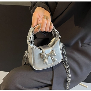 Close-up of a mini silver metallic bow bag with a delicate chain strap held by a model