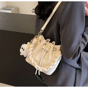Close-up of cream bucket bag with woven handle, fuzzy pompom charm, and crossbody strap