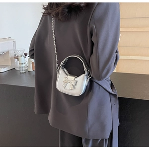 Close-up of a silver bow crossbody bag with metallic finish and chain strap on a model
