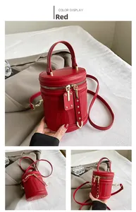 Detail of red cylindrical bucket bag with vertical stripes, gold zippers and handles