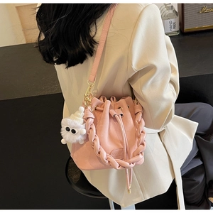 Pink bucket bag with drawstring, woven handle, and cute plush charm shown on model