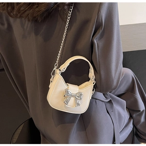 Detail of cream crossbody bag featuring a shiny silver metallic bow and chain strap