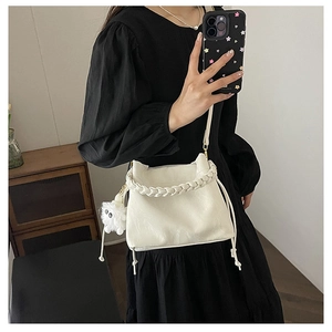 Détail du sac seau blanc crème avec poignée tressée et pompon en peluche sur un modèle