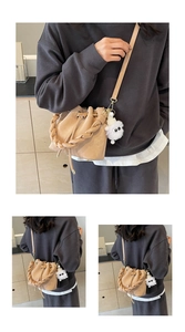 Detail view of beige drawstring bucket bag with braided handle and plush charm on strap