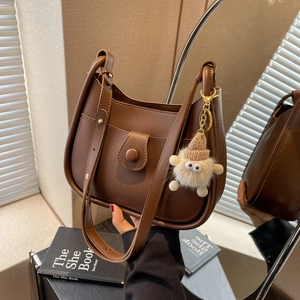 Dark brown saddle shoulder bag with plush charm and magnetic buckle closure