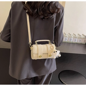 Detail of cream cylindrical leather handbag with gold twist locks and plush bear charm