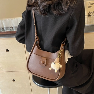 Brown semi-circular crossbody bucket bag with a cute plush charm and adjustable strap