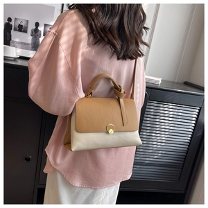Detail of a chic two-tone handbag featuring a gold ring lock and tan flap closure