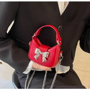 Close-up of mini red crossbody bag featuring silver metal bow and fine chain strap