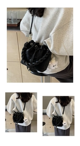 Close-up of black bucket bag with woven handle and plush monster charm detail