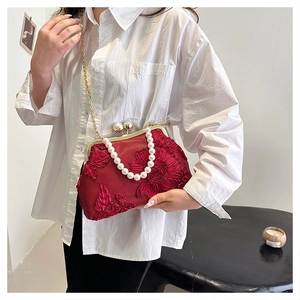 Close-up of red satin kiss-lock bag featuring 3D floral embroidery and pearl handle