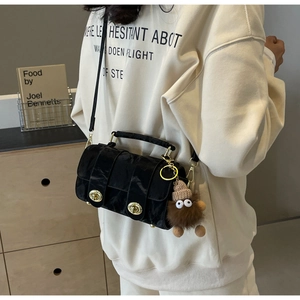 Detail of black pleated glossy crossbody bag with gold clasps and cute monster charm