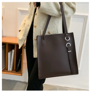 Side view of dark brown tote bag with silver ring buckle on model wearing cream jacket