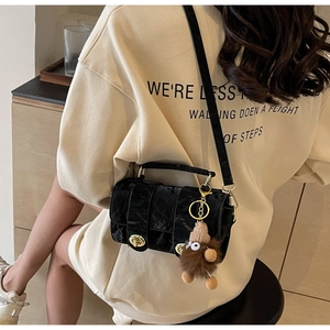 Close-up of black textured crossbody bag with gold hardware and plush bear charm