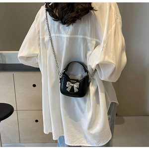 Close-up of a black mini crossbody bag with a silver metal bow and fine chain strap