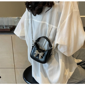 Detail of black mini crossbody bag featuring a large silver bow and metallic chain strap