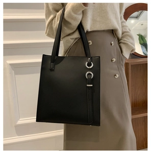 Detail of black faux leather tote bag featuring silver metal rings and chic side straps