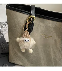 Close-up of a plush monster charm with a knit hat hanging on a khaki tote bag
