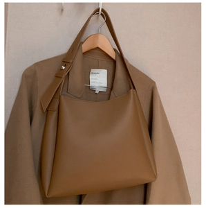 Close-up of dark camel tote bag strap with metal buckle hanging on a brown coat
