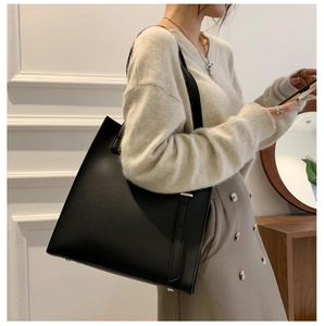 Detail view of large black leather tote bag with fine shoulder straps on a model