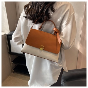 Detail of color-block shoulder bag with caramel flap and gold circular buckle closure